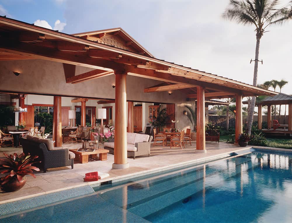 Elegant outdoor living area of a custom timber frame home, showcasing exposed wood beams, handcrafted timber posts, and seamless indoor-outdoor design overlooking a tropical landscape